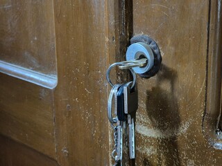 Set of keys hanging from keyhole in old wooden door with scratched surface