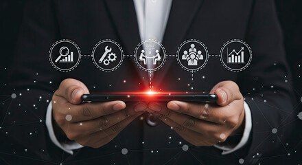 Businessman holding a smartphone displaying a chain of business management and workflow icons over a dark background