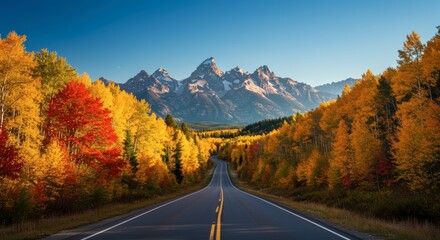 Scenic highway leads towards mountain range surrounded by vibrant autumn foliage under clear blue sky