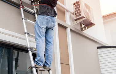 Fototapeta premium Worker climbing up metal ladder on wall at outdoor, closeup. Repairman worker standing on ladder.
