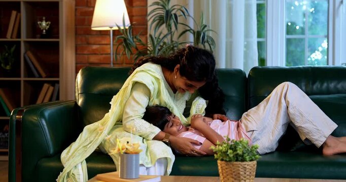 Indian mother tickling son while sitting in modern home on sofa, bonding in quality time together, sharing laughter, affection, love, joy, warmth, parent child relationship, family lifestyle indoors