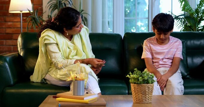 Indian mother scolding son while sitting in modern home on sofa, teaching good habits, inculcating discipline, bonding in quality time, guiding child with love, parent child relationship indoors