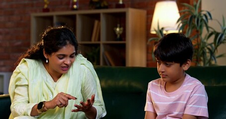 Indian mother scolding son while sitting in modern home on sofa, teaching good habits, inculcating discipline, bonding in quality time, guiding child with love, parent child relationship indoors