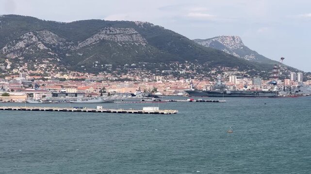 Panoramic wide shot of the French Navy base featuring docked warships and the Charles de Gaulle aircraft carrier in Toulon, Provence, France.