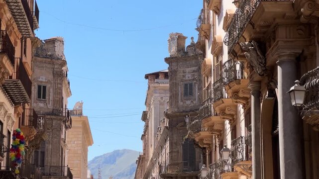 Low angle forward tracking shot walking looking up at the ornate Sicilian Baroque facades, balconies, and columns in the historic center of Palermo, Italy.