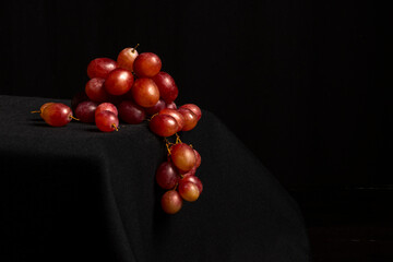 Close-up of a bunch of red grapes on a table and a black background, horizontally with copy space