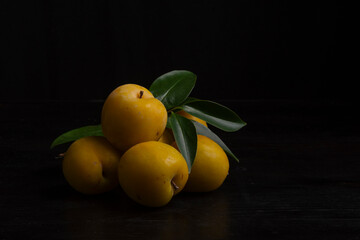 Group view of yellow plums with green leaves, on a black background, horizontally with copy space