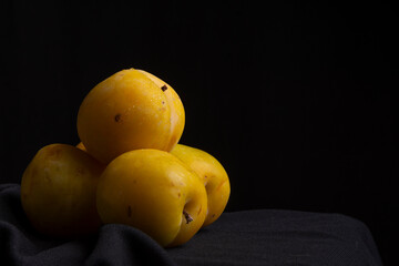 Close-up of yellow plums with drops, on a cloth and black background, horizontally with copy space
