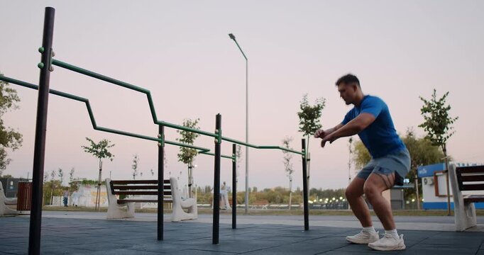 A man is executing a series of squats at an outdoor gym that features parallel bars