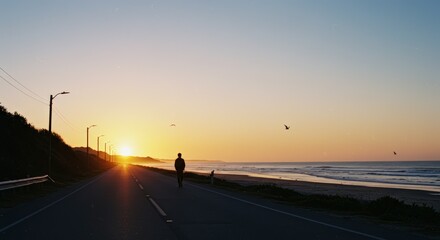 Silhouette of a person walking along a coastal road at sunset with scenic ocean views and sky