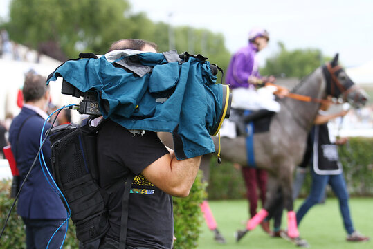 Operador de c&aacute;mara con protector de equipo y funda en d&iacute;a de lluvia grabando carreras de caballos en el hip&oacute;dromo