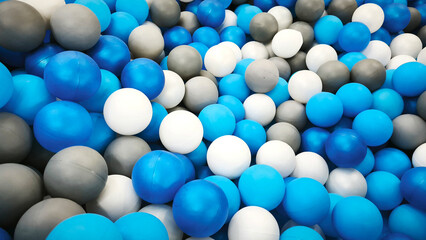 Colorful plastic balls in a play pool, featuring blue, white, and gray shades. Fun indoor playground detail, perfect for kids parties, recreation, and festive celebrations. Background