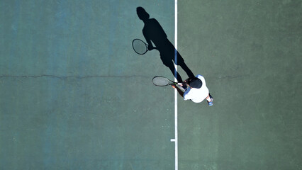Tennis player in white practices on a hardcourt, aerial shot. Focuses on skill development and...