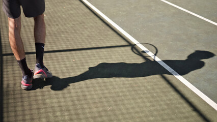 Tennis player practicing on a hardcourt, highlighting focused training. Shadow and racket emphasize dedication and precision.
