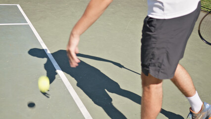 Tennis player practicing on a hardcourt, focused on ball control. Dressed in athletic attire, the athlete demonstrates skill and precision.