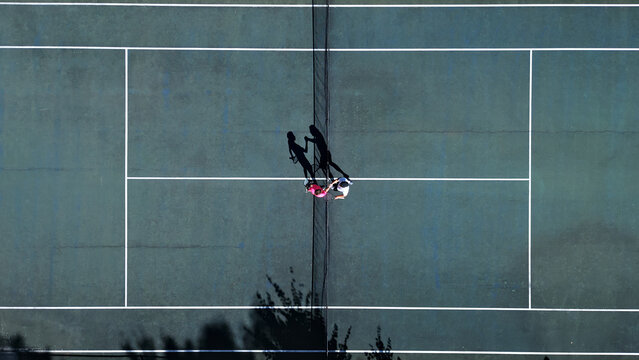 Two players practice doubles tennis on a hardcourt, focusing on strategy. Aerial drone shot highlights their net positioning, teamwork, and skill development in a professional training setting.