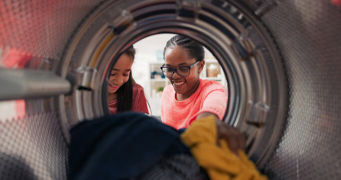 A cheerful daughter helps her mom with the laundry, holding clothes in her hands while the woman opens the washing machine drum, they enjoy spending time together.