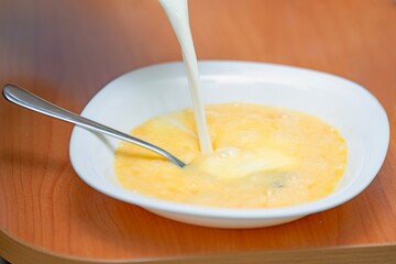 Pouring milk into beaten chicken eggs to prepare mixture for making an omelette