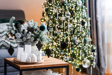 New Year's decor in the interior. White ceramic houses, a spruce bouquet, and candles on the table in the living room. The concept of preparing the house for Christmas.