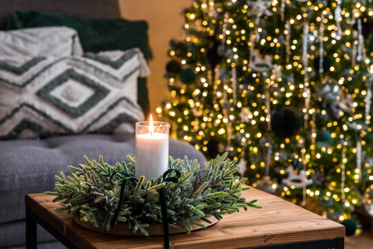 A candle on the table in the living room and a Christmas wreath. New Year's decor in the interior. The concept of preparing a house for Christmas and New Year. Christmas Eve.