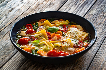 Italian ravioli soup with vegetables on wooden table