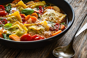 Italian ravioli soup with vegetables on wooden table