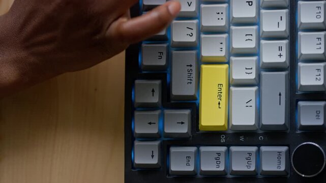 Top view close-up of hands of anonymous black woman typing symbols on desktop computer keyboard and pressing yellow enter key, while logging into system or typing password