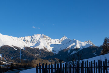 Majestic Snow-Covered Alpine Peaks and Forest with Wooden Fence in Foreground