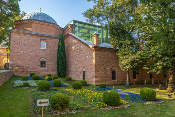 Exterior of Muradiye Madrasa in Bursa with brick walls, domed roof, colorful garden and historic Ottoman architecture.