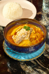 Authentic Thai Sour Curry with Sea Bass (Gaeng Som) Served with Steamed Jasmine Rice in a Restaurant Setting
