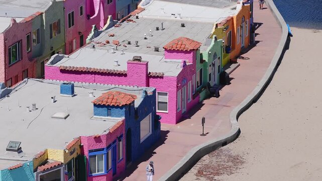 Aerial view of pastel colored buildings with red tiled roofs in Capitola, California. A bridge with vehicles and pedestrians adds motion to the scene.