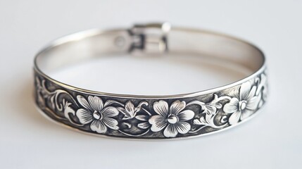 A handcrafted silver bracelet with engraved floral patterns displayed on a solid white background detailed etching visible under soft 