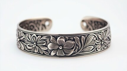 A handcrafted silver bracelet with engraved floral patterns displayed on a solid white background detailed etching visible under soft 