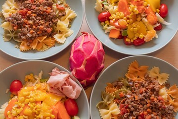 Variety of homemade meals. Bowls with farfalle pasta and beef ragù, fresh corn salad with lettuce, peppers, tomatoes and ham. Healthy lifestyle, balanced diet and home cooking concept.