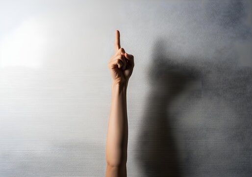 Female hand pointing upward with index finger raised against light concrete wall background in vertical gesture