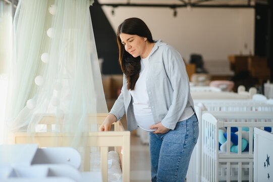Smiling pregnant woman choosing baby crib at shopping mall