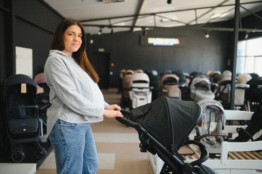 Young pregnant woman in shop of children goods. The choice for a baby stroller