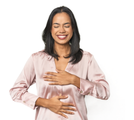 Simple portrait of a young Latina laughs happily and has fun keeping hands on stomach.