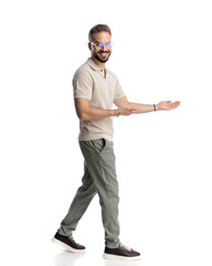 proud young man with glasses smiling and inviting to side while walking