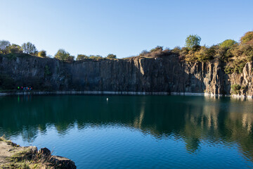 Majestic rock faces frame the deep, emerald pool of the quarry. The cold water contrasts starkly with the rugged sandstone cliffs at Prestonhill Quarry, Inverkeithing, Fife, Scotland.
