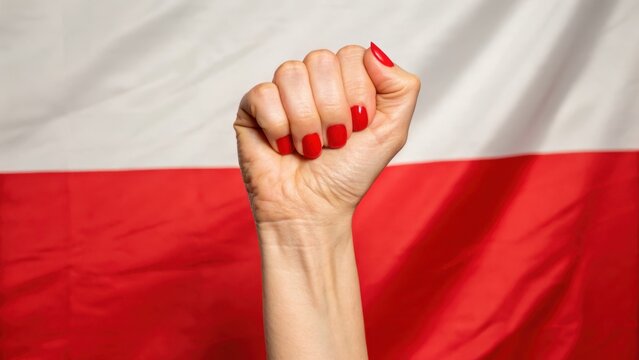 polish freedom fight Raised fist with red nail polish against a backdrop of a Polish flag.
