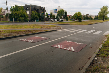 Modular speed bumps (speed bumps) of red color with white reflective elements, installed on an asphalt road in a residential area or on the outskirts of the city.