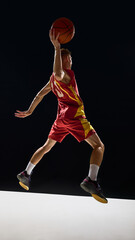 Obraz premium Basketball player in red and yellow uniform flying with ball above head in emotional action. Concept of sports branding, posters, education visuals, fitness lifestyle, and powerful design.