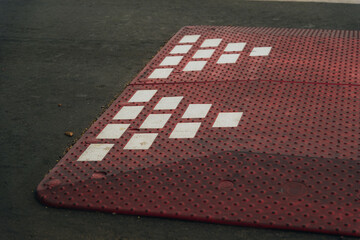 Modular speed bumps (speed bumps) of red color with white reflective elements, installed on an asphalt road in a residential area or on the outskirts of the city.