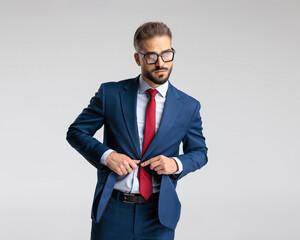 sexy young businessman with glasses looking to side and unbuttoning suit