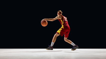 Basketball player in red jersey dribbling ball with intensity on dark court. Concept of determination, sports branding, youth energy, and promotional advertising visuals. © master1305
