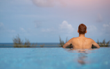Tourist relaxing in infinity pool overlooking tropical ocean