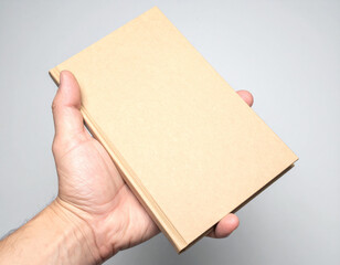 Obraz premium A person's hand holding a plain, unadorned brown book against a neutral gray background, highlighting the simple object