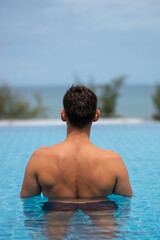 Tourist relaxing in infinity pool overlooking tropical ocean