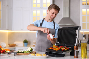 Man adding salt to vegetables cooking on electric grill in kitchen